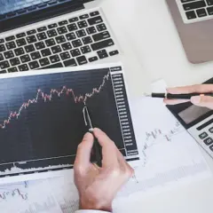 Analiza wykresów akcji co to jest? Dłonie wskazują na wzrosty na papierze wartościowym, obok kalkulator i laptop.