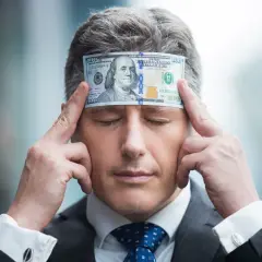 Biznesmen z banknotem 100 dolarów na czole, zamyślony nad tym, jak pomnażać pieniądze.