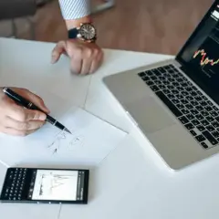 Analiza wykresów na laptopie i telefonie, notatki na papierze. To może być przygotowanie do gry na giełdzie, jak na stooq.