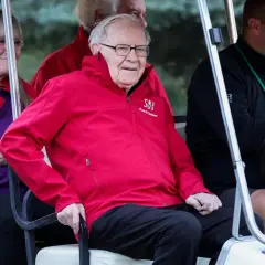 Warren Buffett w czerwonej kurtce z logo Allen & Company, siedzi w golfowym wózku.