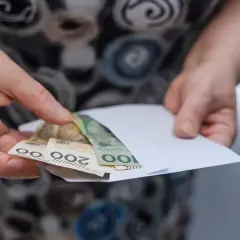 Dłonie trzymają kopertę z pieniędzmi. Tabela emerytura brutto netto.