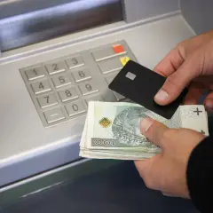 Ręce trzymające kartę i banknoty przy bankomacie, pokazujące, jak wpłacić pieniądze na konto.