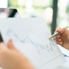 Analiza wykresu to klucz do tego, jak kontrolować emocje w pracy. Dłoń z długopisem wskazuje na dane, symbolizując spokój i opanowanie.