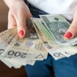 Dłonie trzymające plik banknotów 100 i 200 zł. Czy to kwota, ile zarabia 5 procent najbogatszych Polaków?
