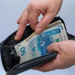 Dłonie wkładają banknoty 50 zł do portfela. Czy mam 58 lat i mogę przejść na emeryturę?