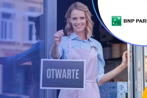 Uśmiechnięta kobieta w fartuszku wiesza tabliczkę "OTWARTE". Obok logo banku BNP Paribas.