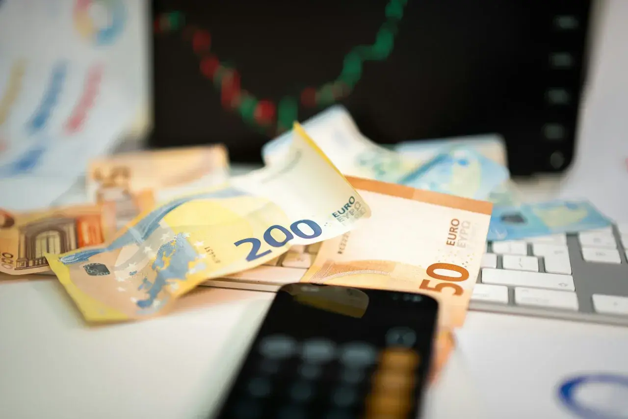 Euro banknoty na klawiaturze, telefon i wykres giełdowy sugerują, jak inwestować w waluty.