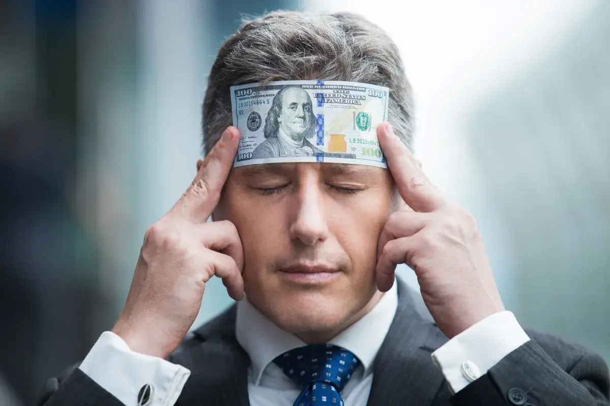 Biznesmen z banknotem 100 dolarów na czole, zamyślony nad tym, jak pomnażać pieniądze.