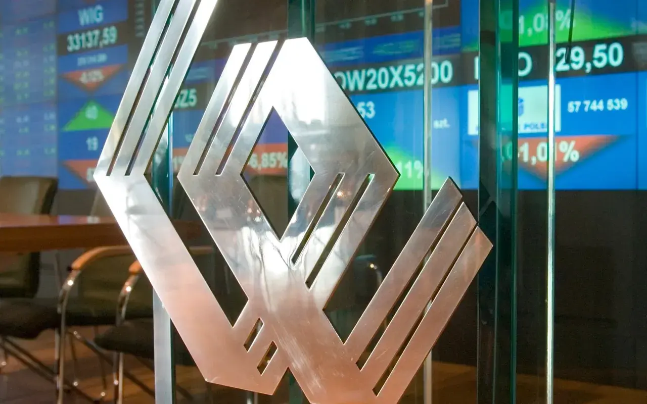 Metalowe logo na tle ekranów giełdowych. Asbis rekomendacje widać na wykresach.