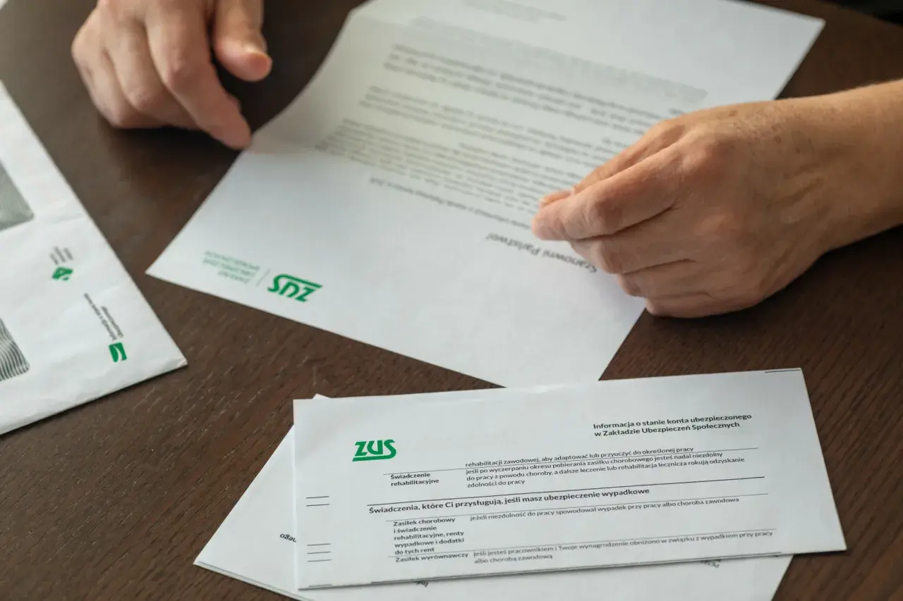 Dłonie przeglądają dokumenty ZUS. Informacje o świadczeniach i tym, jak przejść na emeryturę, są kluczowe.
