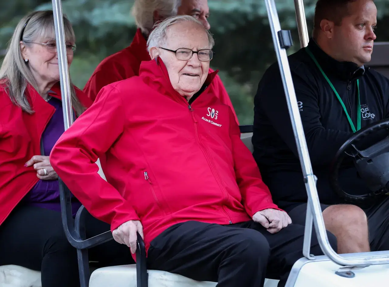 Warren Buffett w czerwonej kurtce z logo Allen & Company, siedzi w golfowym wózku.