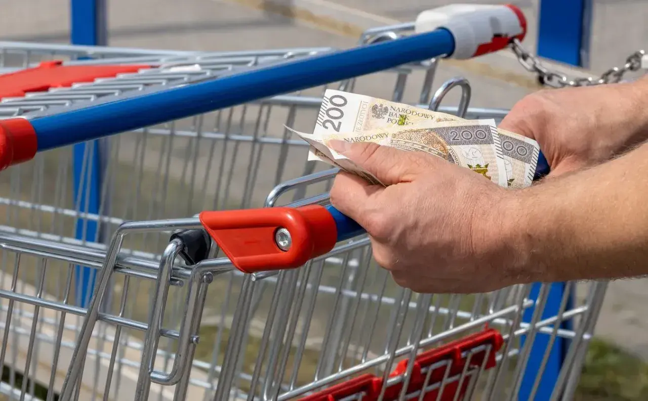 Ręce trzymają banknoty 200 zł przy wózku sklepowym. Kto zyskuje na inflacji, gdy ceny rosną?