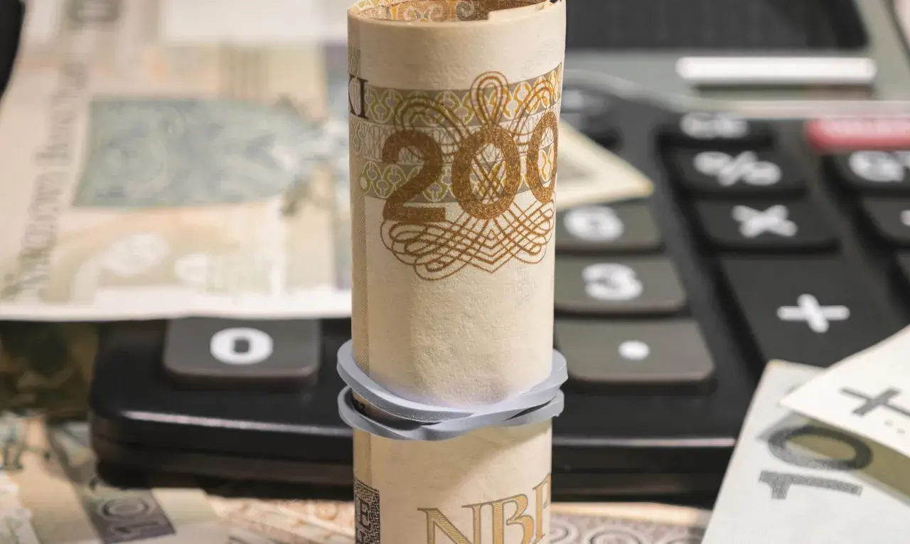 Zrolowany banknot 200 zł na kalkulatorze, obok inne nominały. Analiza millenium kurs akcji.