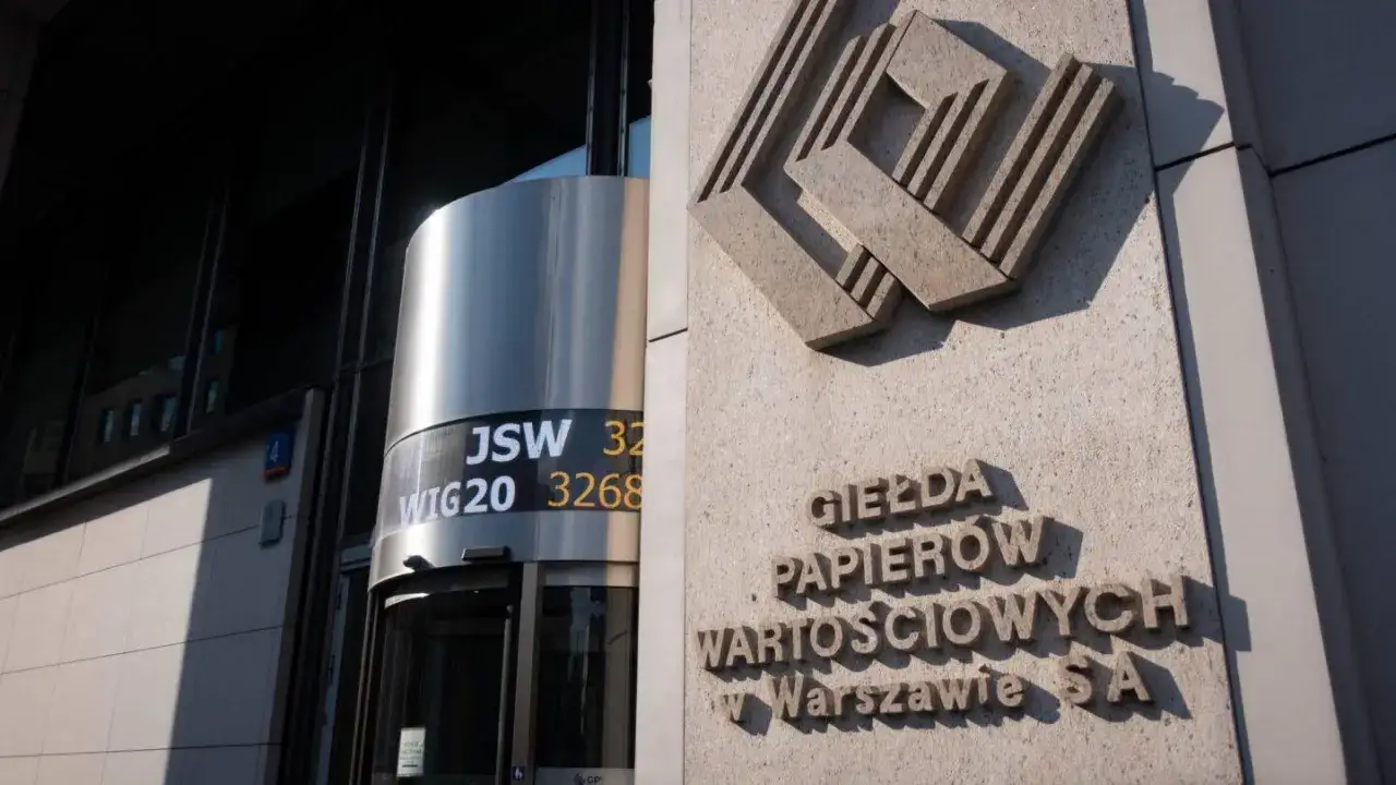 Giełda Papierów Wartościowych w Warszawie. Na budynku widnieje logo i napis. Obok wejścia wyświetlane są dane, w tym WIG20 akcje.